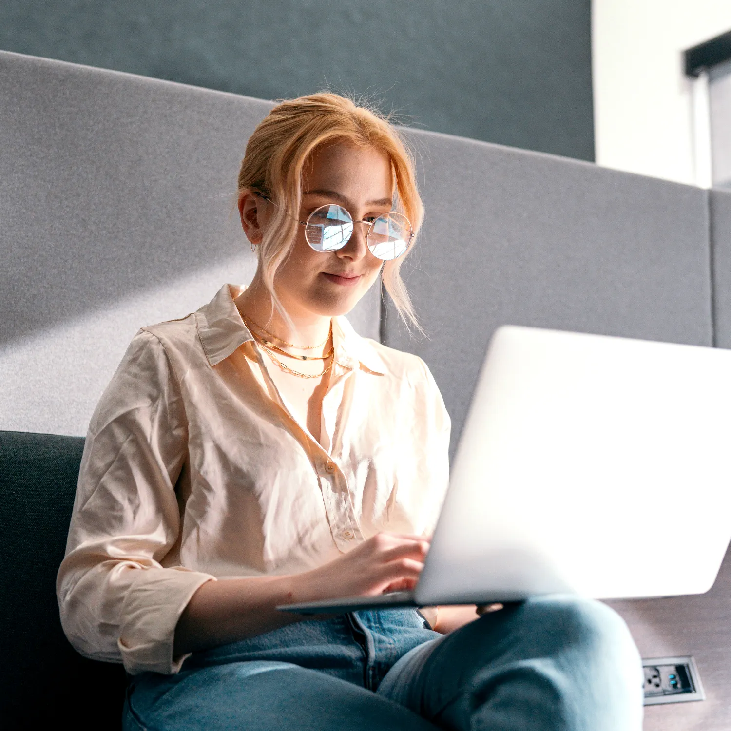 Junge Frau mit runder Brille sitzt auf einem Sofa und arbeitet konzentriert am Laptop. Hochkannt