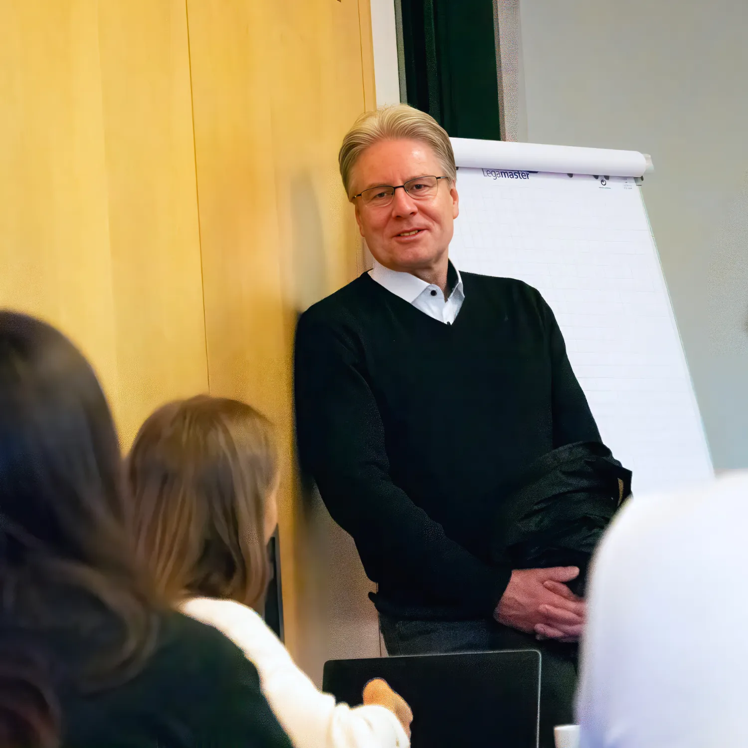 Personalvorstand Porsche Haffner steht lächelnd vor einem Flipchart und spricht zu Teilnehmenden in einem Seminarraum.