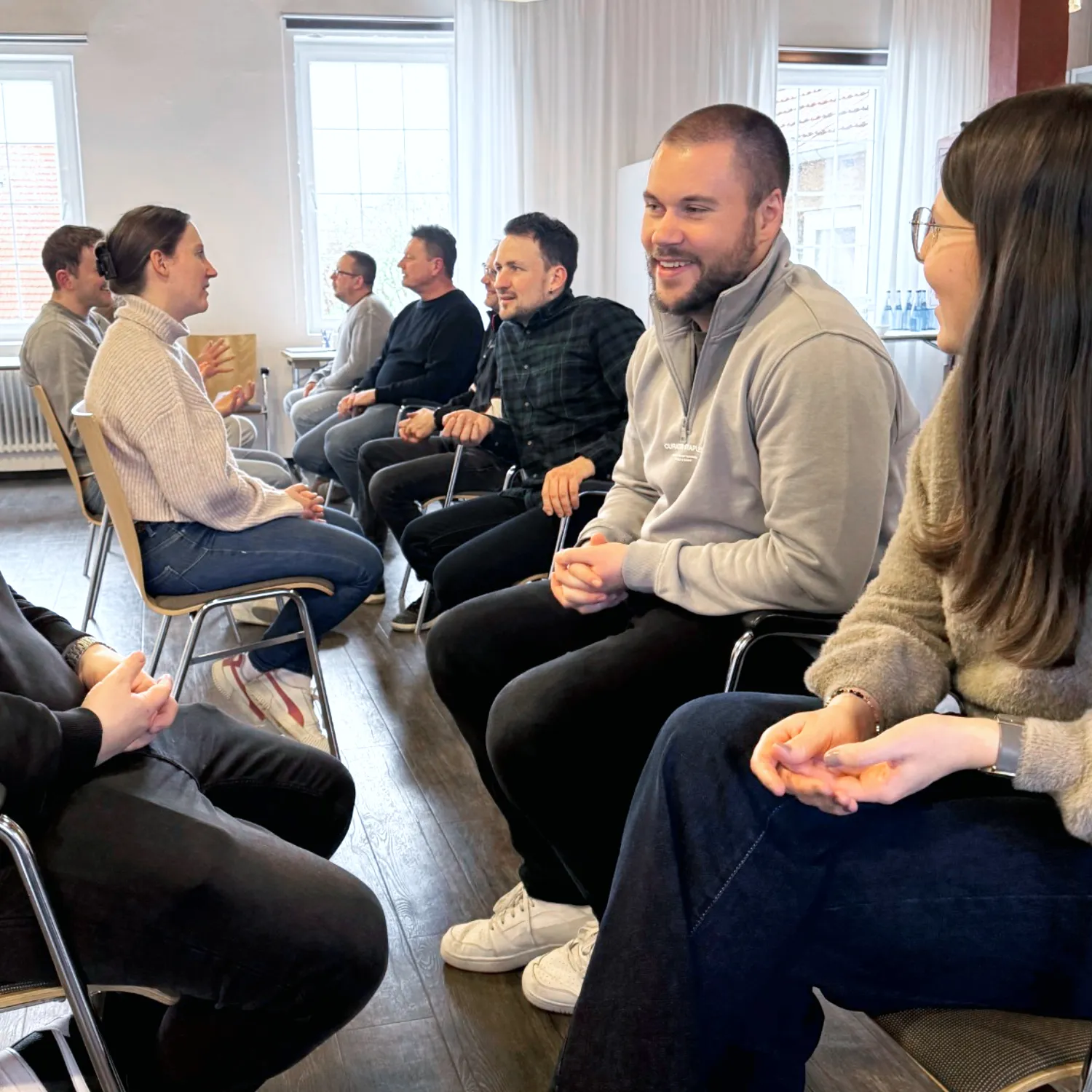 Gruppe von Männern und Frauen nimmt in einem Stuhlkreis an einer interaktiven Workshop-Übung teil.