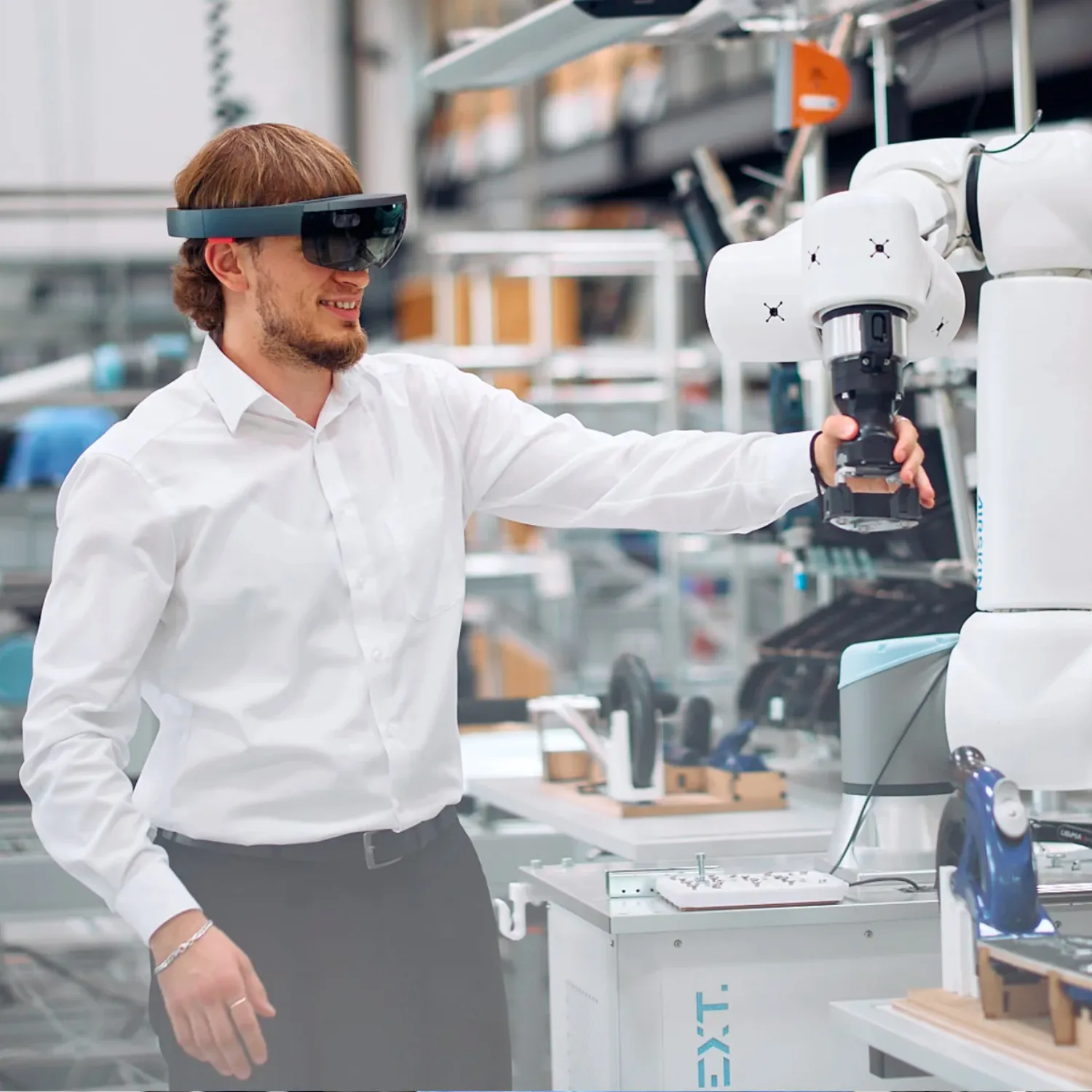 Junger Mann mit AR-Brille interagiert mit einem Roboterarm in einer modernen Industrie 4.0 Halle.